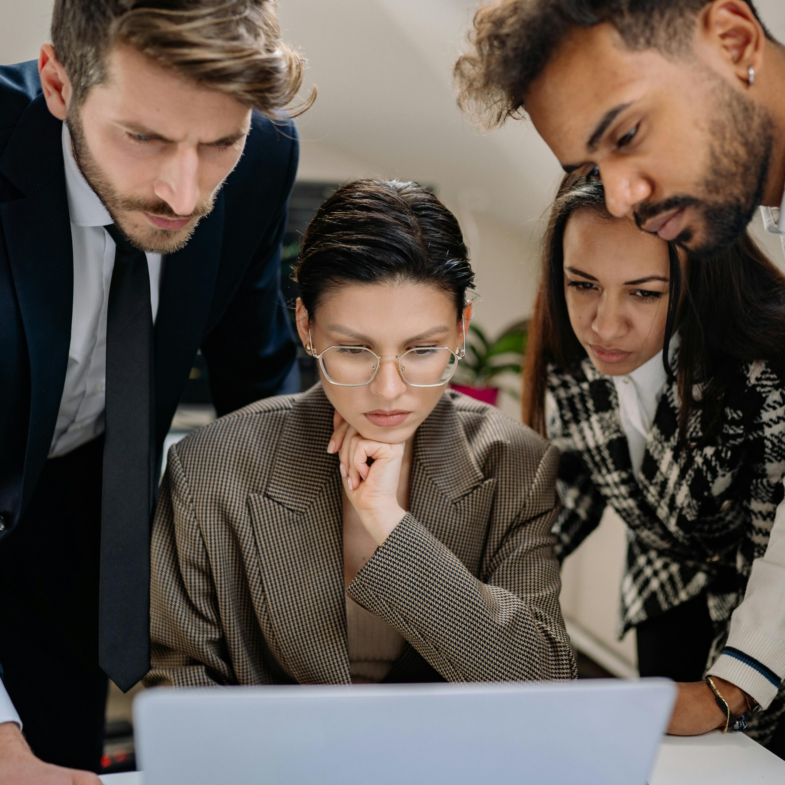 A focused team of four diverse professionals closely examining a laptop screen during a meeting.