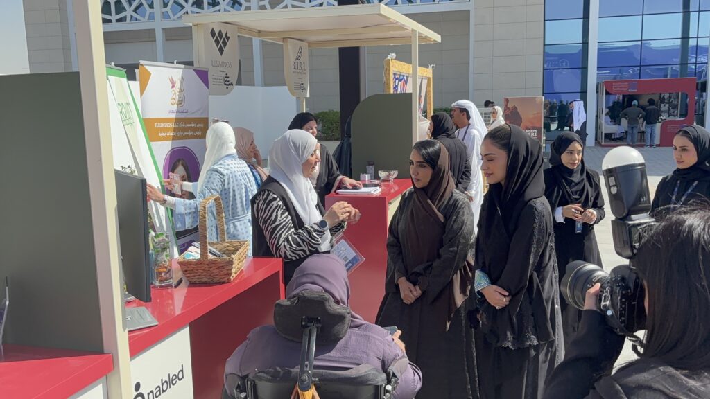 Shuruk El Warrak presenting at an Enabled booth during SEF Sharjah, with attendees gathered around and a wheelchair user in the foreground.